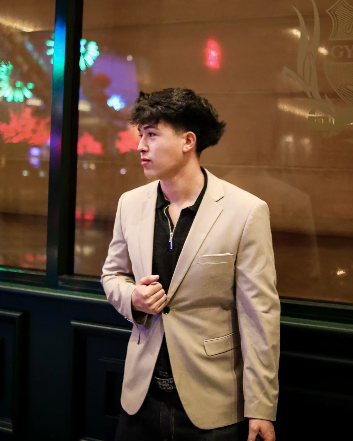 Jordan Lopez in a light blazer, looking out past a window at night